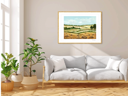 „Fine art tisk letního zlatého pole v přírodním dřevěném rámu zavěšený nad světlou moderní pohovkou v interiéru s pokojovými rostlinami.