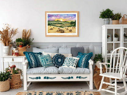 „Fine art tisk Zlaté pole pod soumrakem v přírodním dřevěném rámu zavěšený nad rustikální pohovkou s modrými a bílými dekorativními polštáři, obklopenou rostlinami a dřevěným nábytkem.