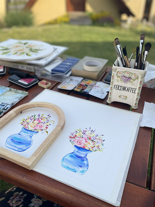 Akvarel květin ve váze na pracovním stole – proces tvorby originální malby, štětce a akvarelové potřeby. Umělecký ateliér Dominiky z Líbezna.